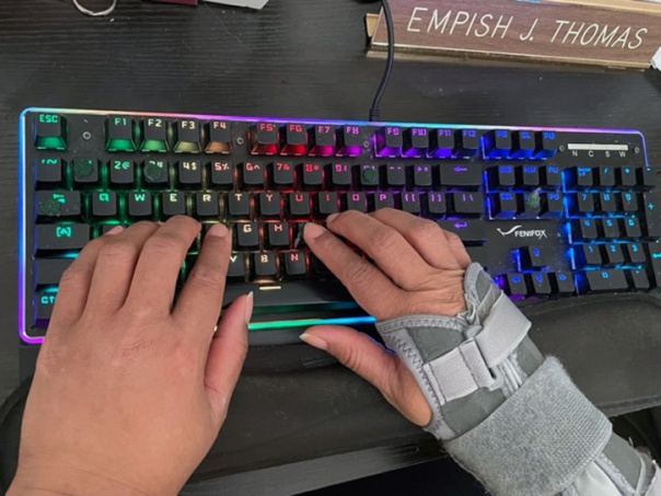Two hands typing on a mechanical keyboard. The right hand is covered in a wrist guard.